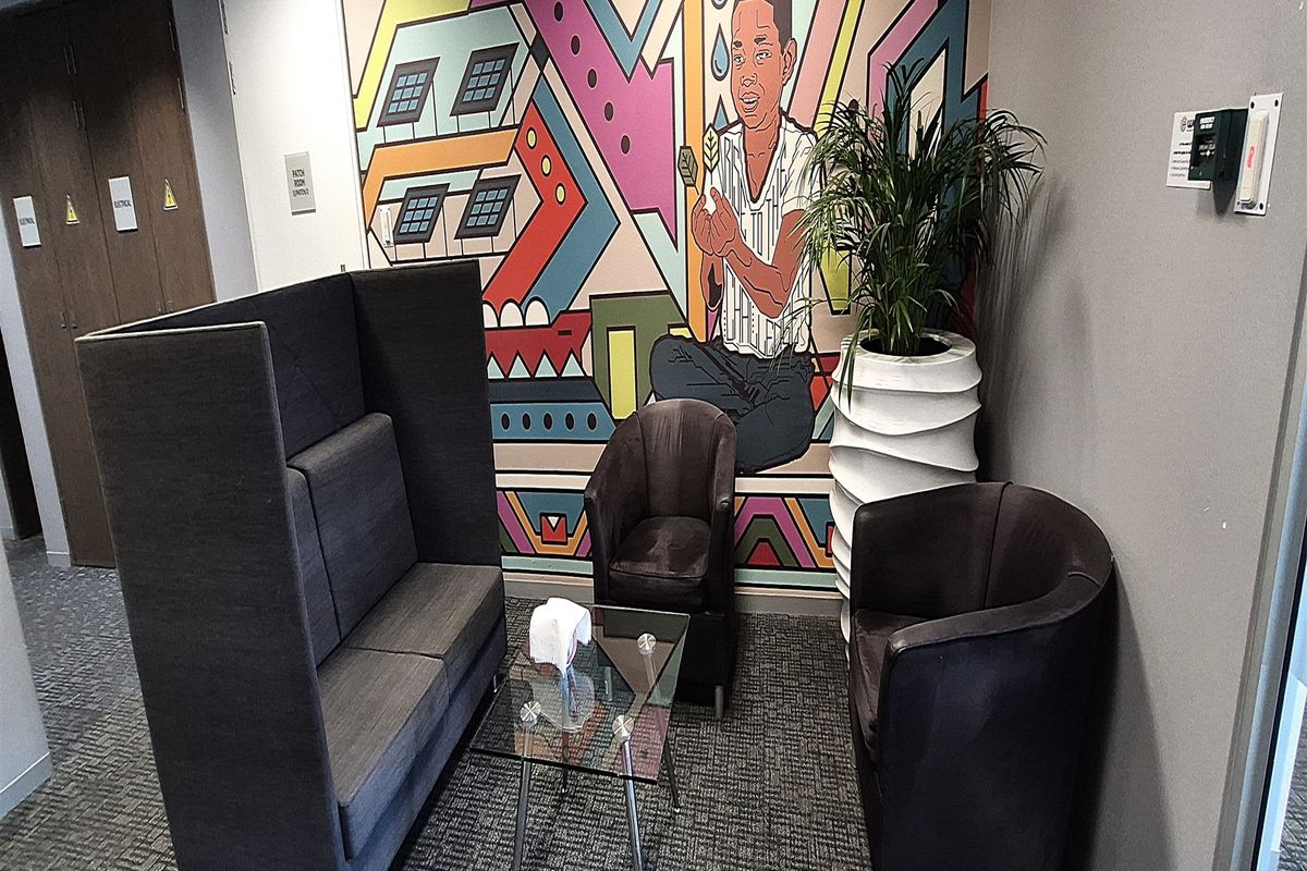A modern office breakout area featuring a vibrant wall mural, carpeted flooring, and professional seating arrangements.