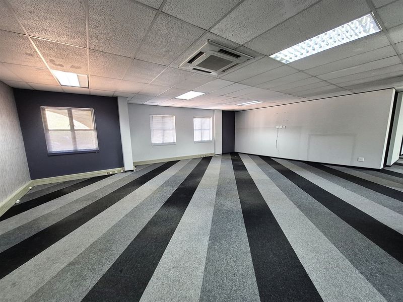 Spacious open-plan office area featuring a suspended ceiling, recessed lighting, integrated air conditioning, and striped carpet flooring.