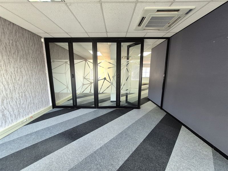 A modern, empty office space featuring a glass partition wall, suspended ceiling with integrated air conditioning, and patterned carpet flooring.