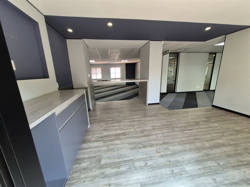 Modern open-plan office space featuring built-in cabinetry, wood-look laminate flooring, recessed lighting, and glass partitions, offering a clean and professional work environment.