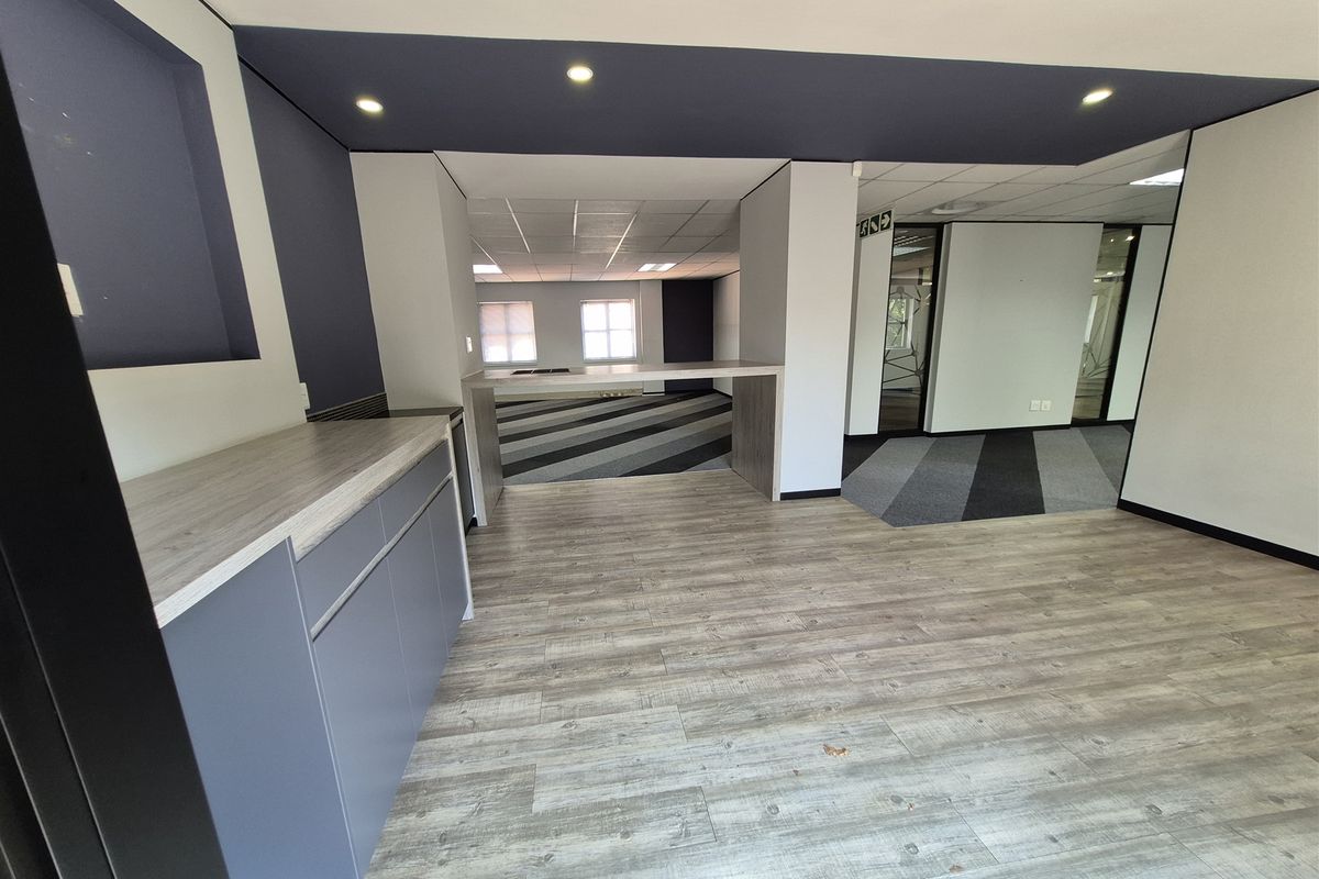 Modern open-plan office space featuring built-in cabinetry, wood-look laminate flooring, recessed lighting, and glass partitions, offering a clean and professional work environment.