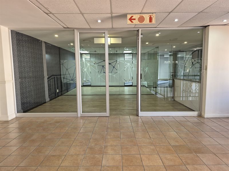 A bright, vacant office space featuring modern glass partitions, laminate flooring, and a professional suspended ceiling with recessed lighting.