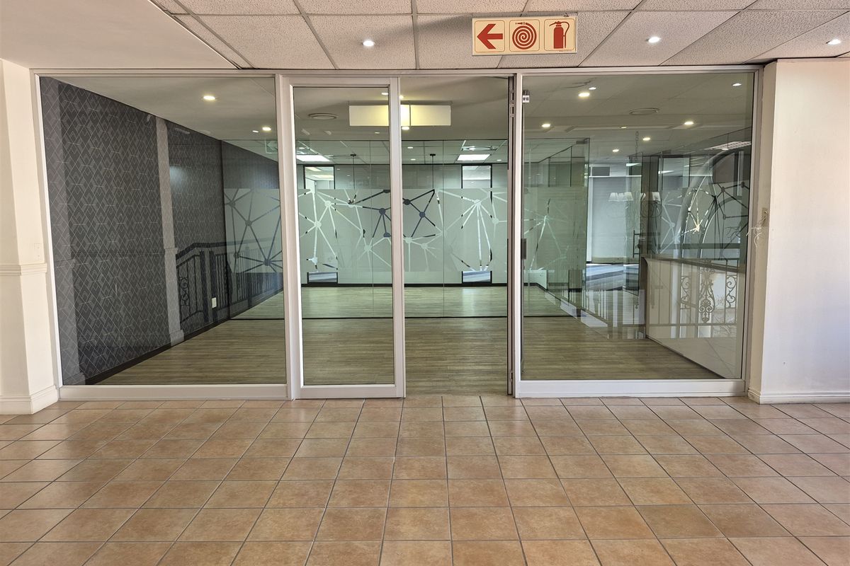 A bright, vacant office space featuring modern glass partitions, laminate flooring, and a professional suspended ceiling with recessed lighting.