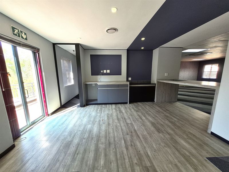 A modern, open-plan office space featuring wood-look laminate flooring, built-in cabinetry, recessed lighting, and a sliding glass door leading to an outdoor area.