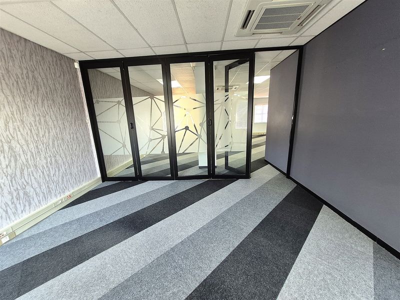 Empty office space featuring a suspended ceiling, recessed air conditioning, glass partition walls, and modern striped carpet tiles.
