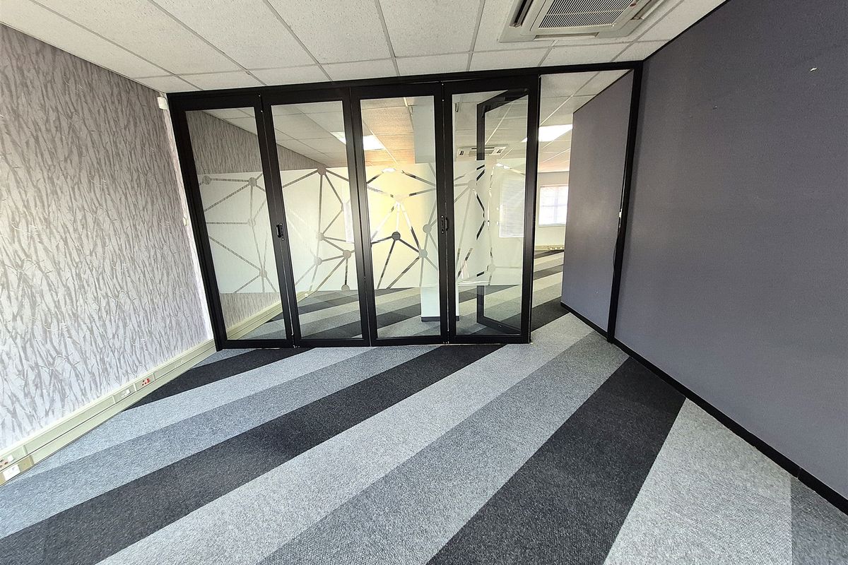 Empty office space featuring a suspended ceiling, recessed air conditioning, glass partition walls, and modern striped carpet tiles.