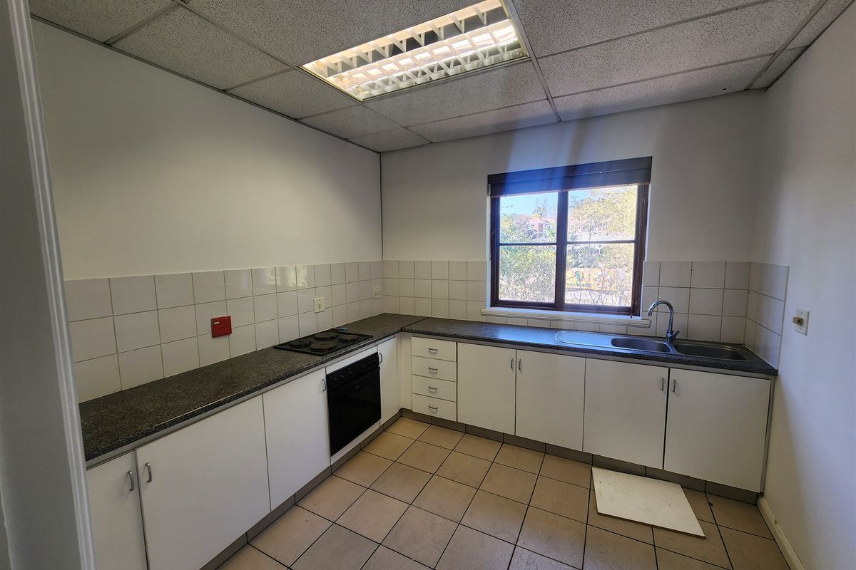 A functional office kitchen featuring white cabinetry, dark laminate countertops, integrated electric hob and oven, and tiled flooring with a drop ceiling.