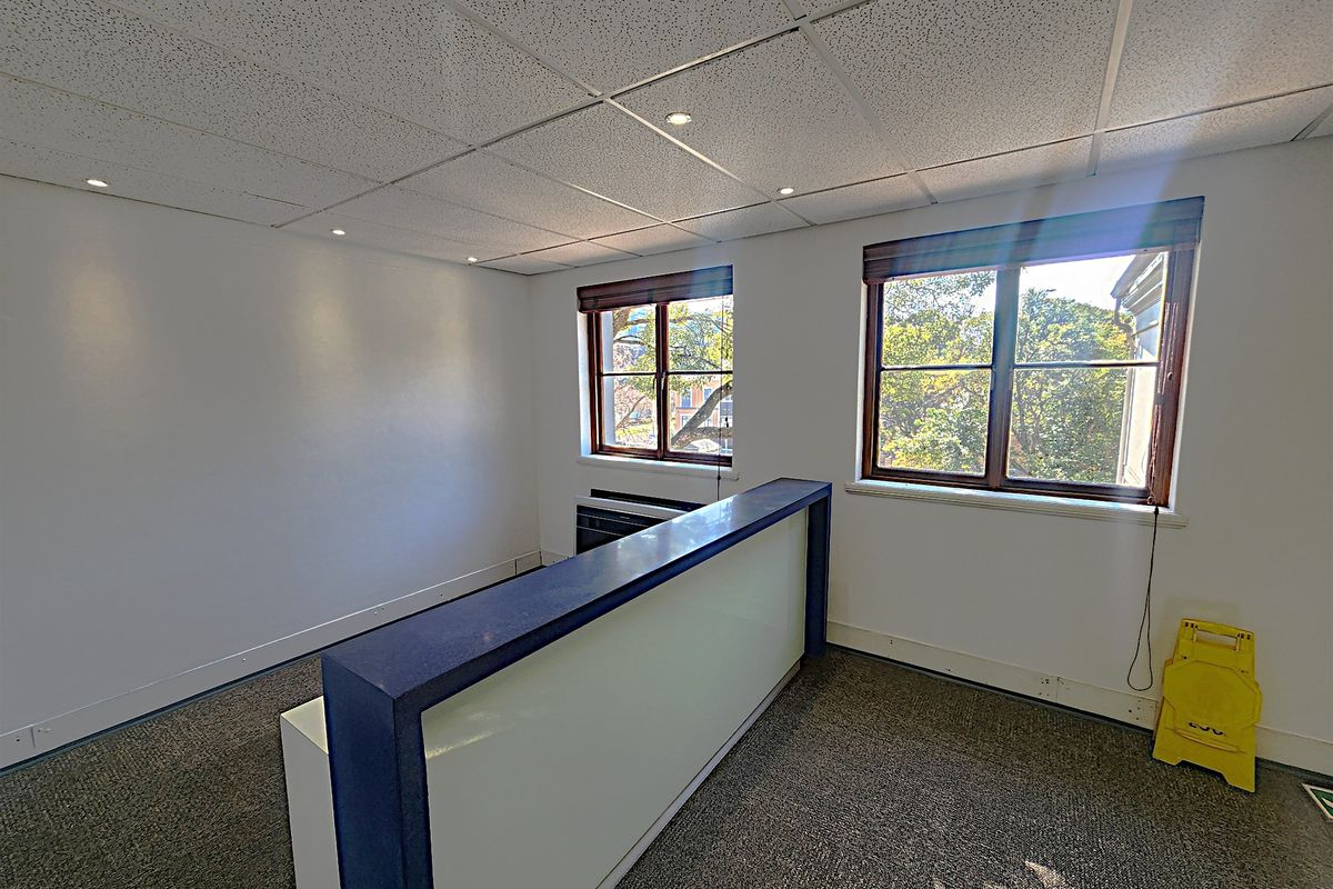 A bright, empty office space featuring a built-in reception desk, carpeted flooring, and large windows providing natural light.