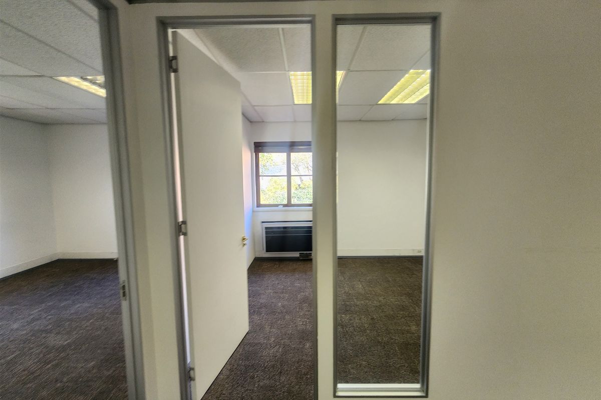 A vacant office space featuring a suspended ceiling, recessed lighting, carpeted flooring, and a glass partition wall with an integrated HVAC unit.