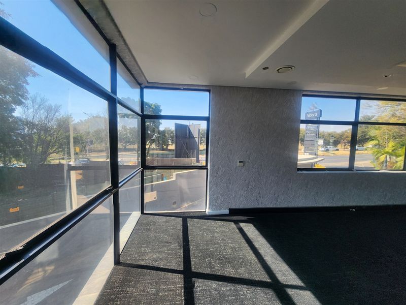 A bright, empty office space featuring large floor-to-ceiling windows, modern carpeted flooring, and a textured feature wall, offering ample natural light.