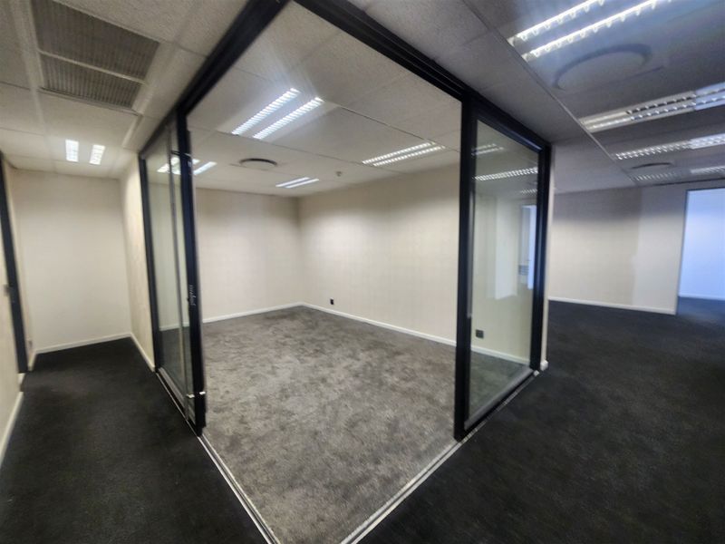 A vacant office space featuring modern glass partitions, carpeted flooring, and a suspended ceiling with integrated lighting.