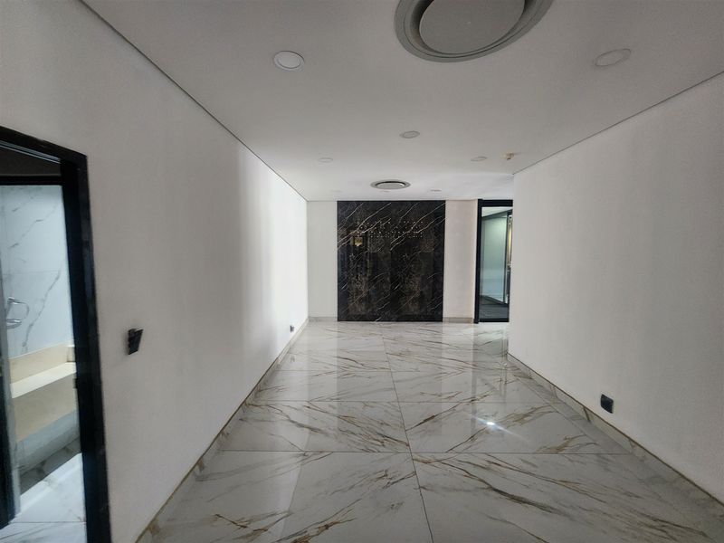 A modern, well-lit hallway featuring polished marble-look floor tiles and a striking black marble feature wall, leading to adjacent office spaces.