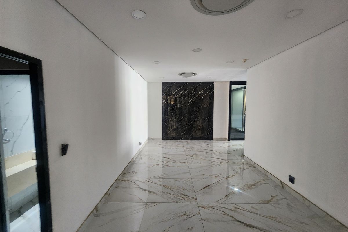A modern, well-lit hallway featuring polished marble-look floor tiles and a striking black marble feature wall, leading to adjacent office spaces.