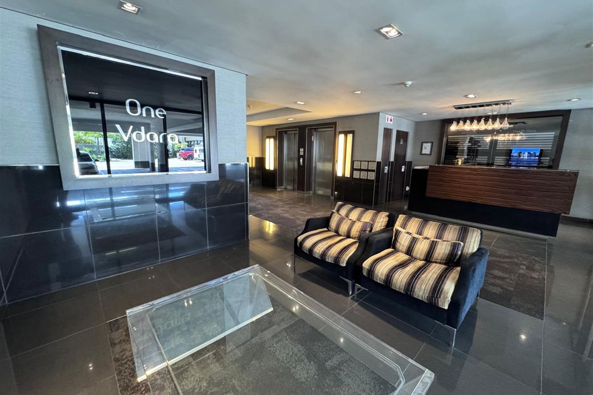 Modern office building lobby featuring a reception desk, elevator access, and polished tiled flooring with professional lighting.