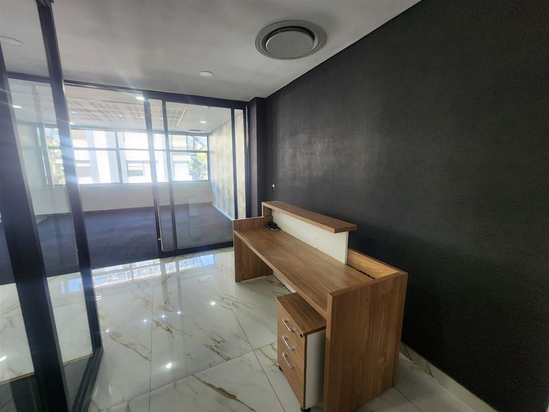 Modern office space featuring marble-look flooring, a built-in reception desk, and a glass partition wall leading to an adjacent workspace.