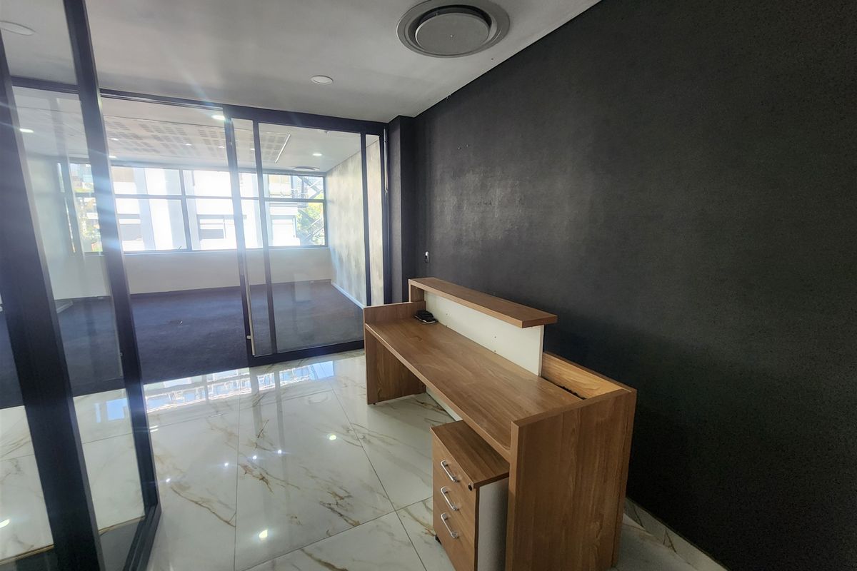 Modern office space featuring marble-look flooring, a built-in reception desk, and a glass partition wall leading to an adjacent workspace.