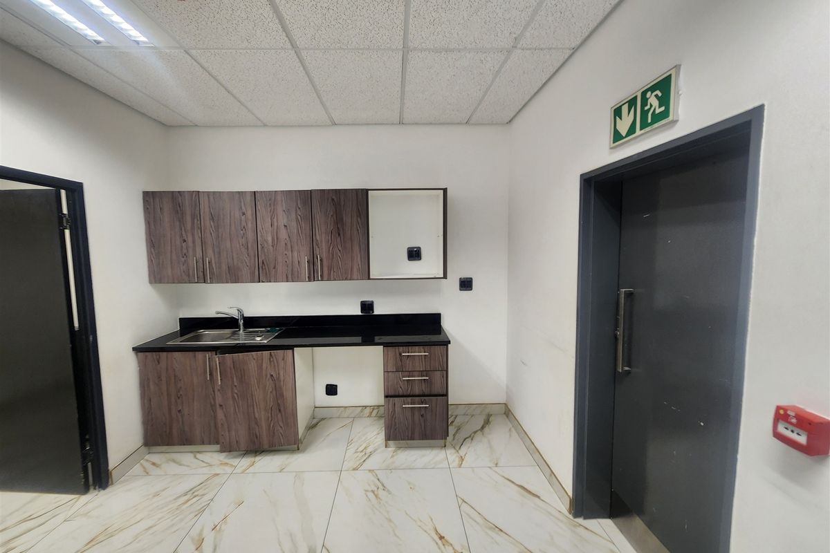 A clean office kitchenette featuring wood-look cabinetry, stone countertops, a stainless steel sink, and modern marble-effect floor tiles.