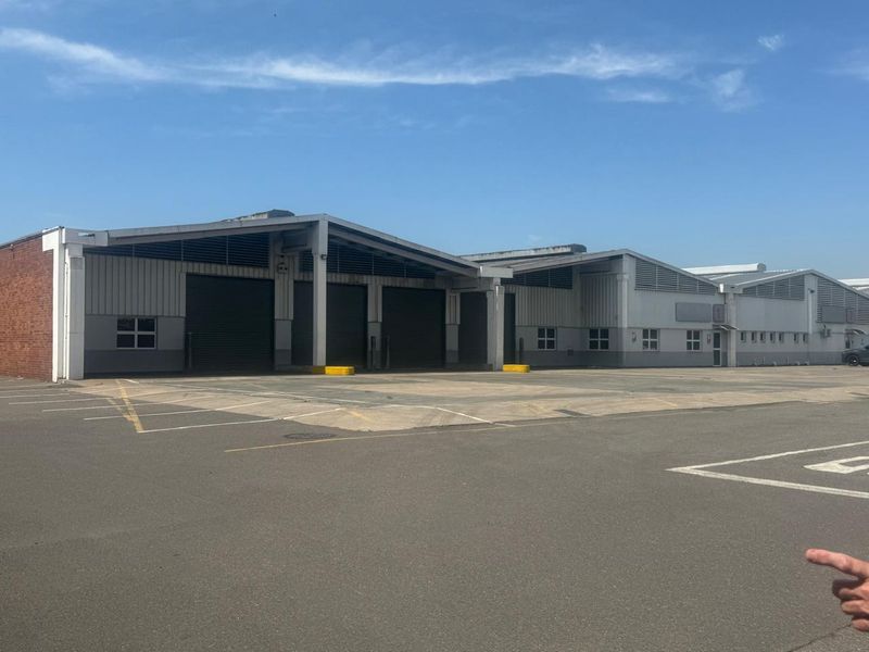 Industrial warehouse facility featuring multiple roller shutter doors, paved loading yard, and steel-framed structure with high-level ventilation.