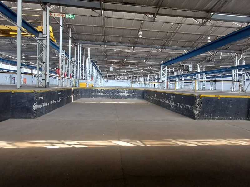 Expansive industrial warehouse interior featuring a large sunken loading dock area, high-clearance steel truss roofing, and robust structural steel support columns.