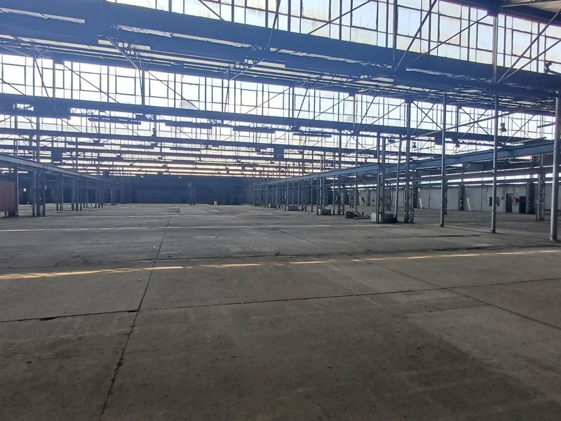 Expansive industrial warehouse space featuring high ceilings, steel structural framework, and large-scale overhead glazing providing significant natural light.