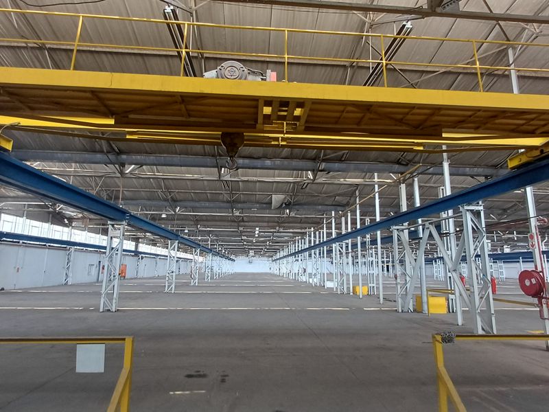 Expansive industrial warehouse space featuring high ceilings, exposed steel trusses, and an overhead gantry crane system for heavy-duty operations.