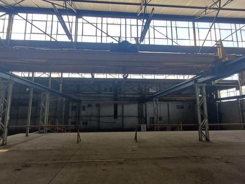 Spacious industrial warehouse featuring high ceilings, large clerestory windows for natural light, and an overhead gantry crane system.