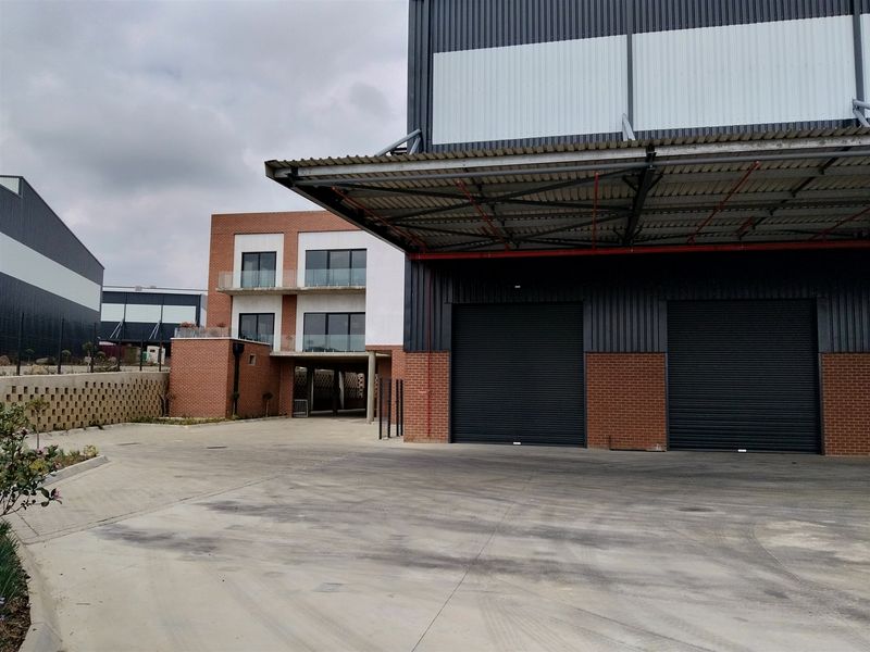 Industrial property featuring a large warehouse with roller shutter doors, a covered loading area, and an adjacent multi-story brick office or residential component.