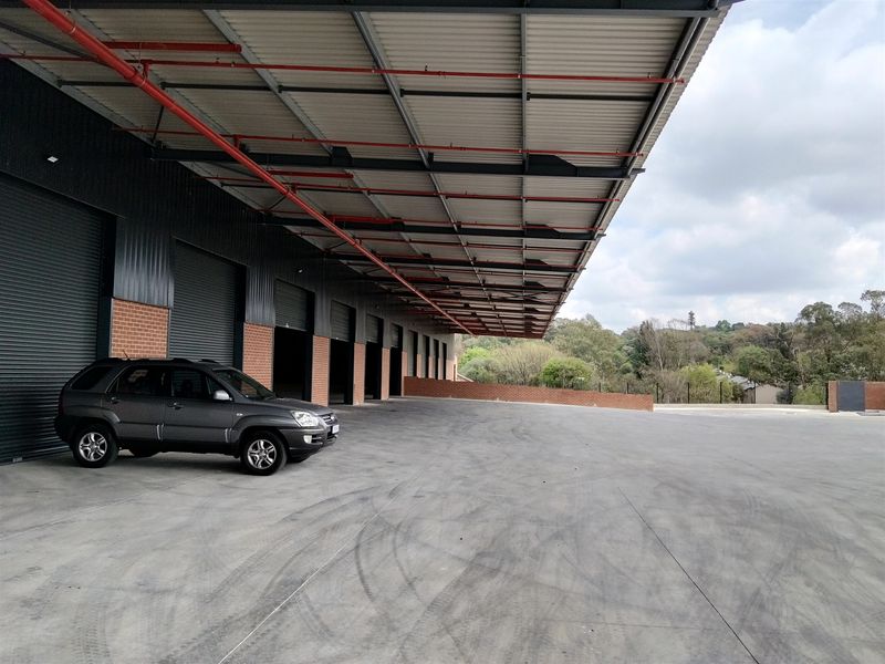 Industrial loading bay area featuring a large concrete hardstand, multiple roller shutter doors, and an extensive covered canopy with integrated fire suppression systems.