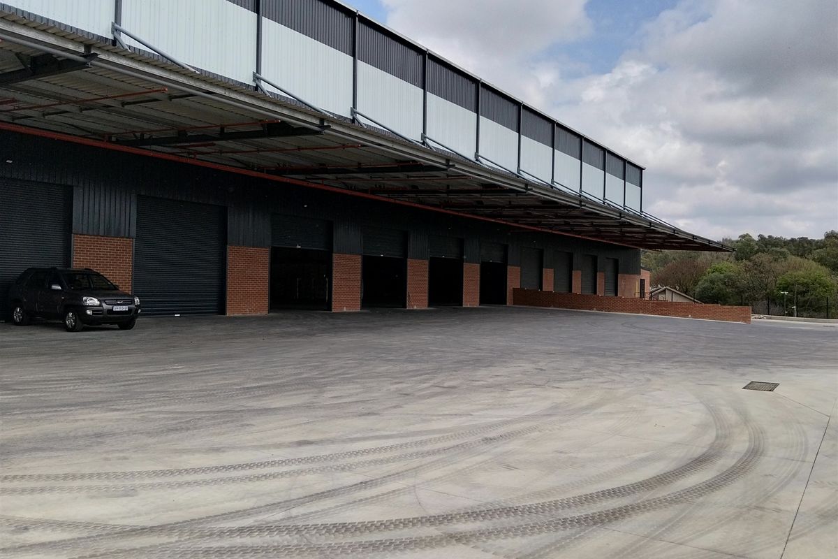 Industrial warehouse exterior featuring multiple roller shutter doors, a large concrete loading yard, and a protective steel canopy.
