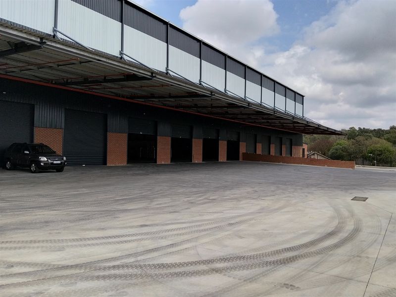 Industrial warehouse exterior featuring multiple roller shutter doors, a large concrete loading yard, and a protective steel canopy.
