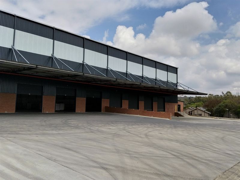 Industrial warehouse exterior featuring multiple loading bays with roller shutter doors, a large concrete hardstand, and a steel canopy structure.