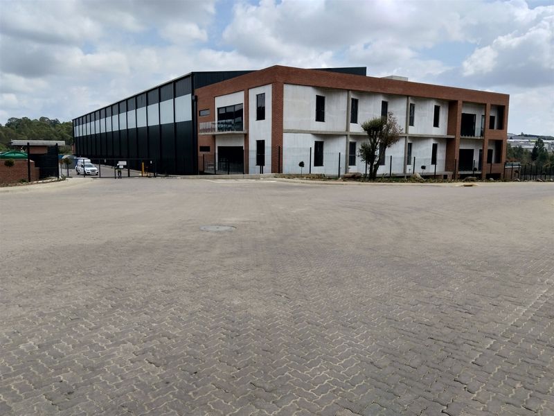 Modern industrial facility featuring a combination of brick and concrete construction with extensive metal cladding and a large paved forecourt area.