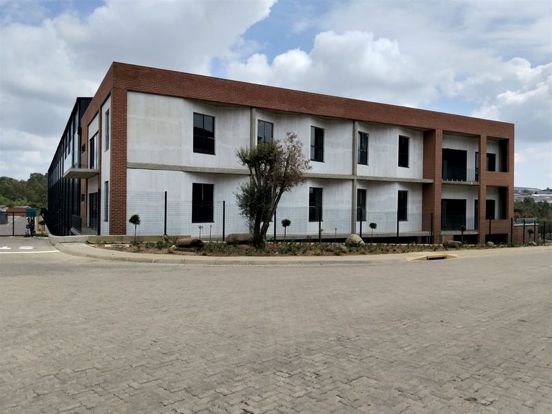 Modern industrial building featuring a combination of red brick and concrete facade with large windows and paved exterior access.