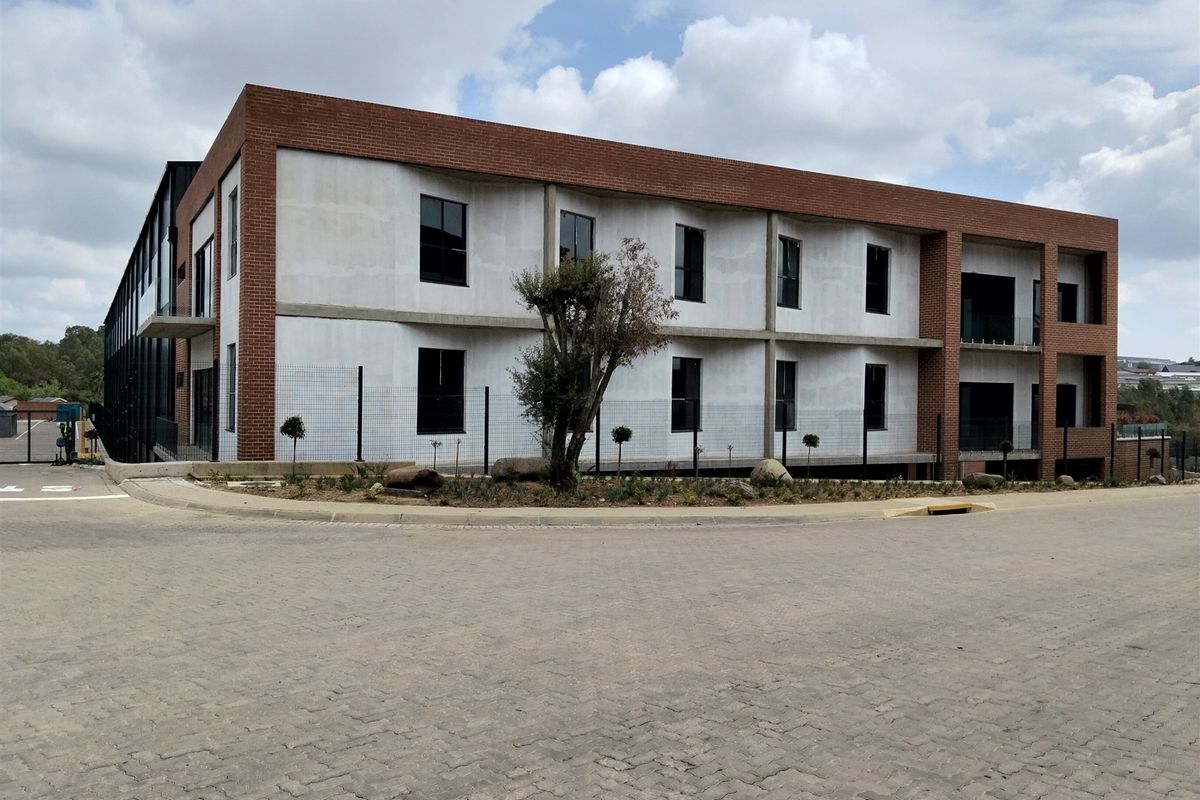 Modern industrial building featuring a combination of red brick and concrete facade with large windows and paved exterior access.