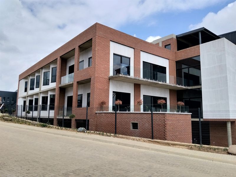 Modern industrial-style multi-story building featuring a face brick facade, concrete balconies with glass balustrades, and large aluminium-framed windows.
