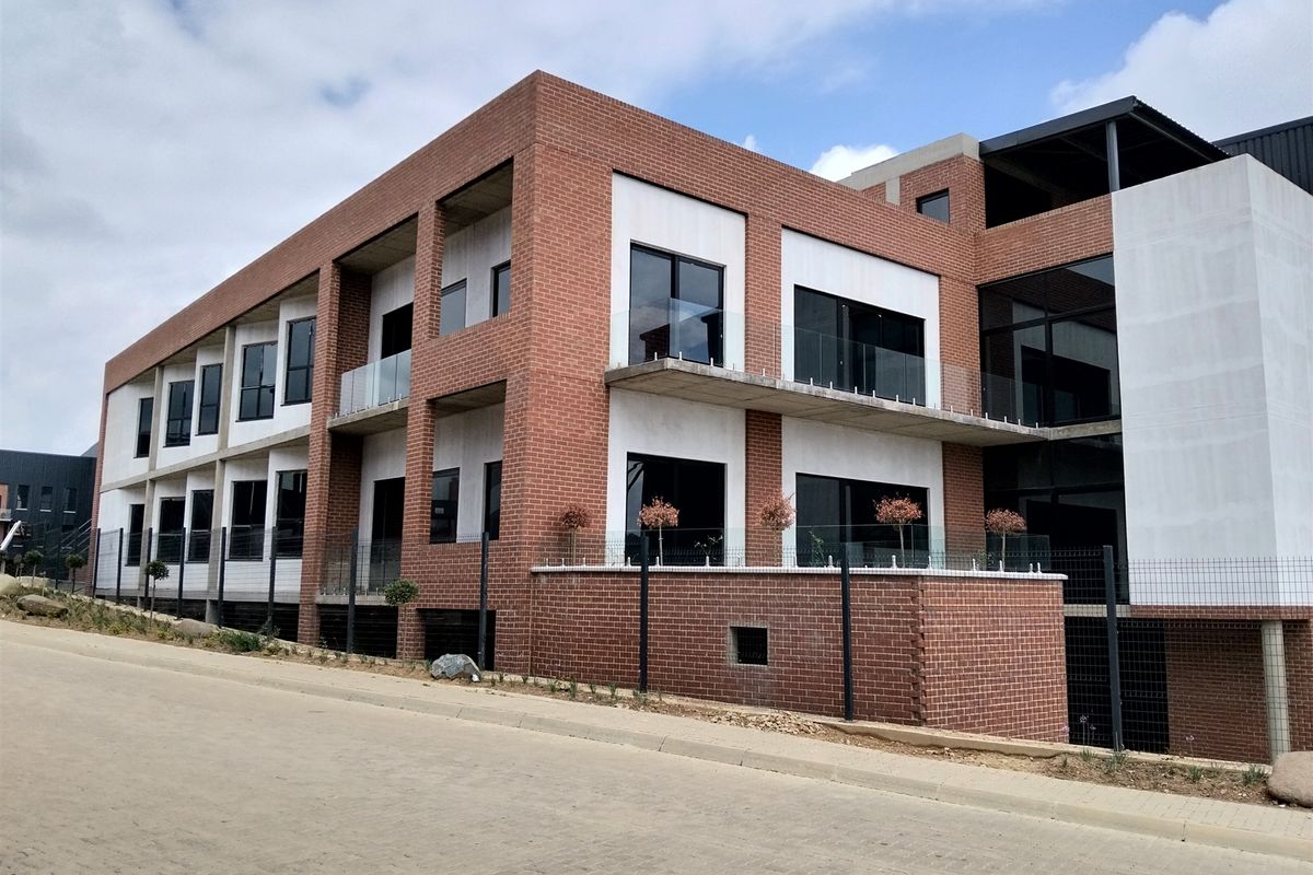 Modern industrial-style multi-story building featuring a face brick facade, concrete balconies with glass balustrades, and large aluminium-framed windows.