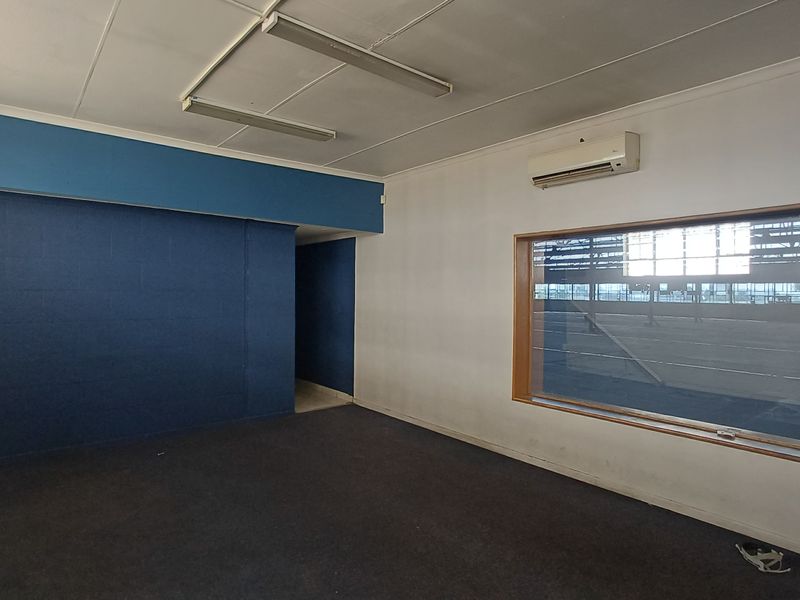 An empty office space featuring a large viewing window, wall-mounted air conditioning unit, and fluorescent ceiling lighting.