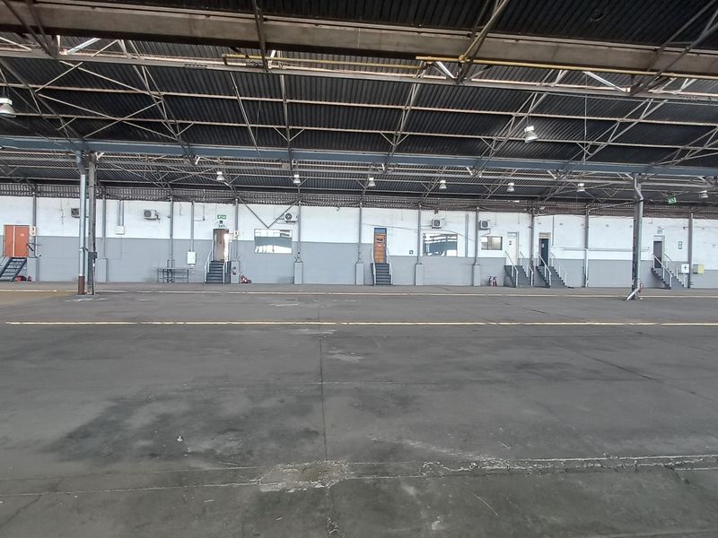 Expansive industrial warehouse space featuring high-truss steel roofing, concrete flooring, and multiple access points with integrated staircases.