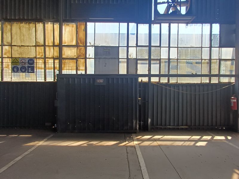 Industrial warehouse interior featuring high-level clerestory windows, metal cladding, and a designated exit point with concrete flooring.