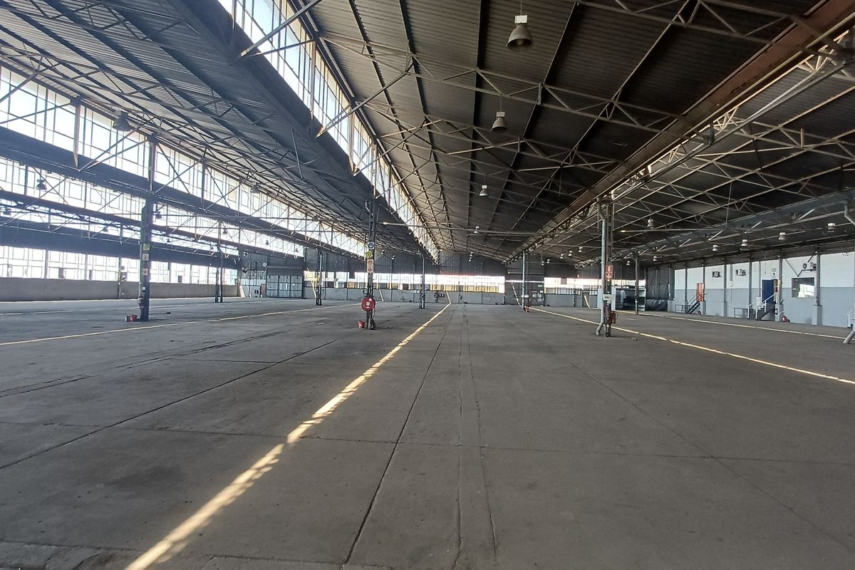 Expansive industrial warehouse space featuring high ceilings, steel truss roofing, large clerestory windows for natural light, and durable concrete flooring.