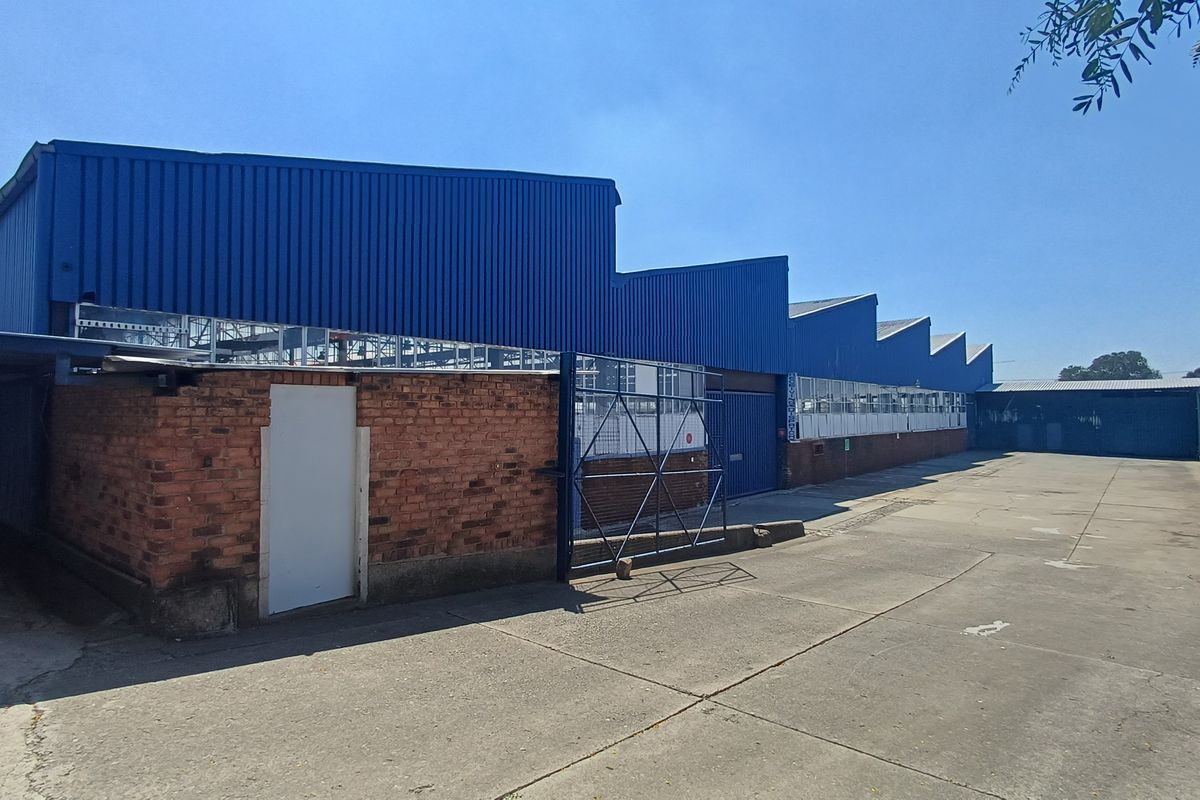 Industrial warehouse exterior featuring a sawtooth roof design, brick and corrugated metal cladding, and a large concrete yard area.