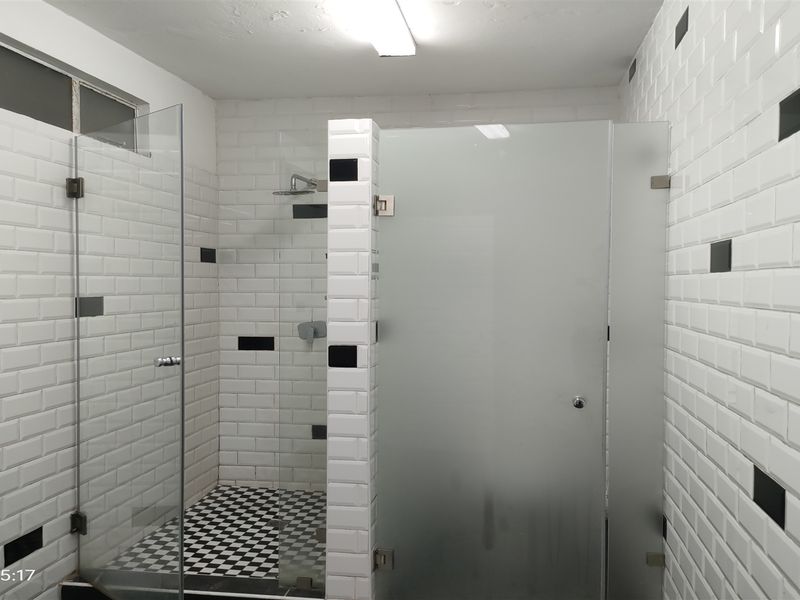 A clean, modern bathroom featuring a glass-enclosed shower with white subway tiles and black accent tiles, complemented by a checkered floor pattern.