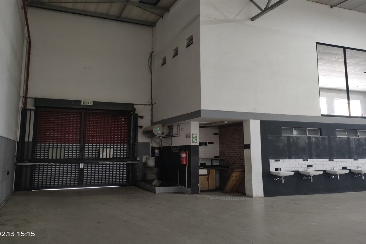 Industrial utility space featuring a large roller shutter door, multiple wall-mounted wash basins with subway tile backsplashes, and an elevated mezzanine area.