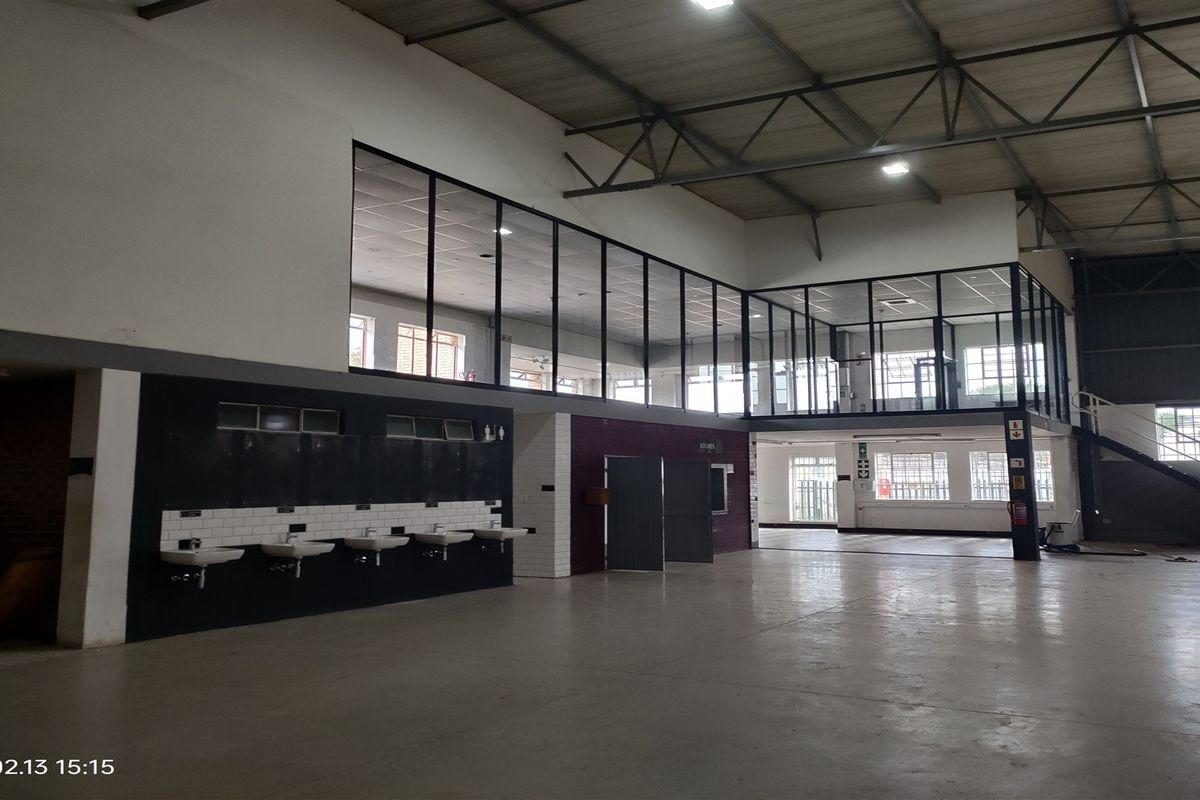 Spacious industrial utility area featuring a mezzanine level with glass partitioning, concrete flooring, and a row of wall-mounted wash basins.