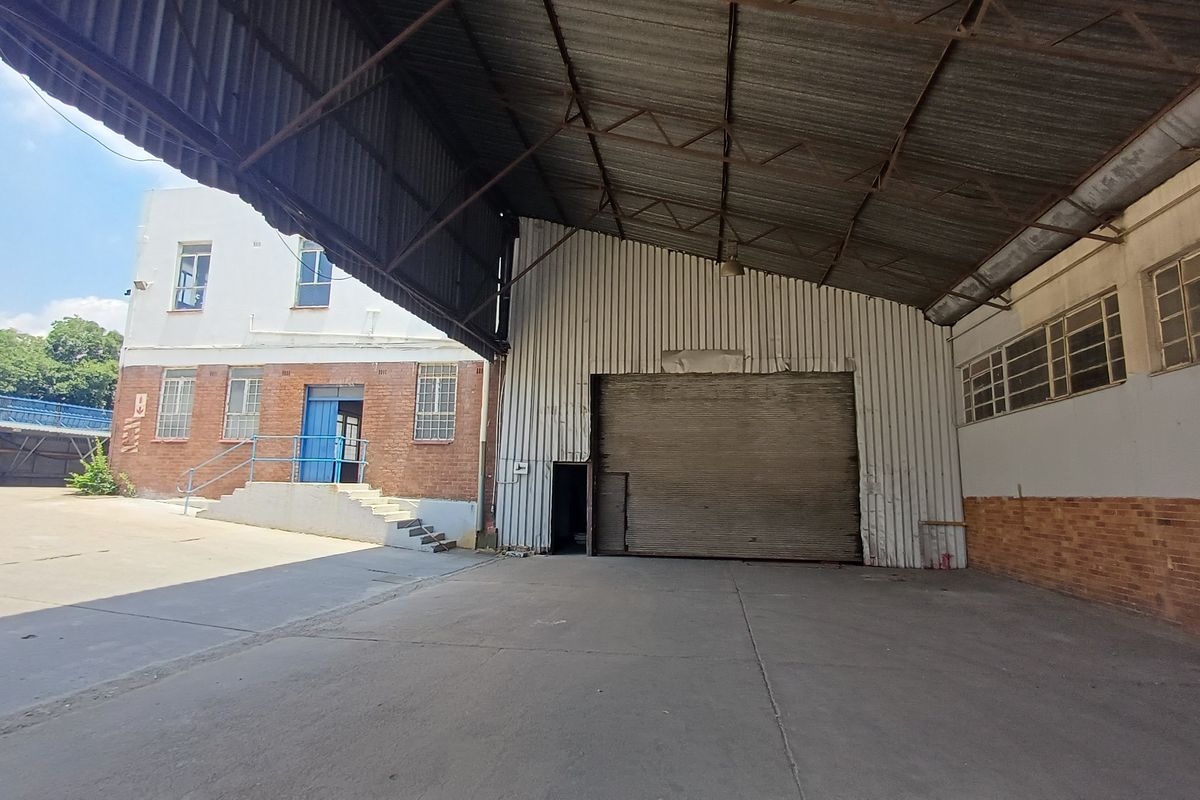 Industrial warehouse space featuring a large covered loading area, high-clearance metal roof, roller shutter door, and adjacent brick office or utility building.