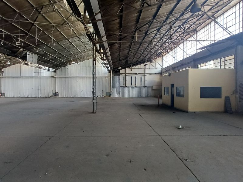 Expansive industrial warehouse space featuring high-clearance steel truss roofing, concrete flooring, and a standalone internal office structure.