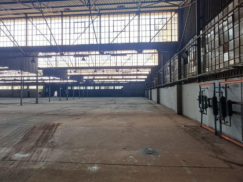 Expansive industrial warehouse space featuring high ceilings, large steel-framed windows, and exposed structural steel trusses, offering significant open-plan floor area.