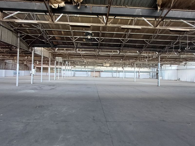 Expansive industrial warehouse space featuring high ceilings, exposed steel truss framework, and large open floor area suitable for storage or manufacturing.