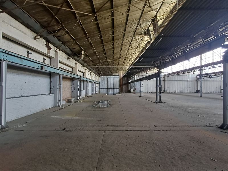Expansive industrial warehouse space featuring high-clearance steel truss roofing, concrete flooring, and exposed structural steel columns, suitable for large-scale storage or manufacturing operations.