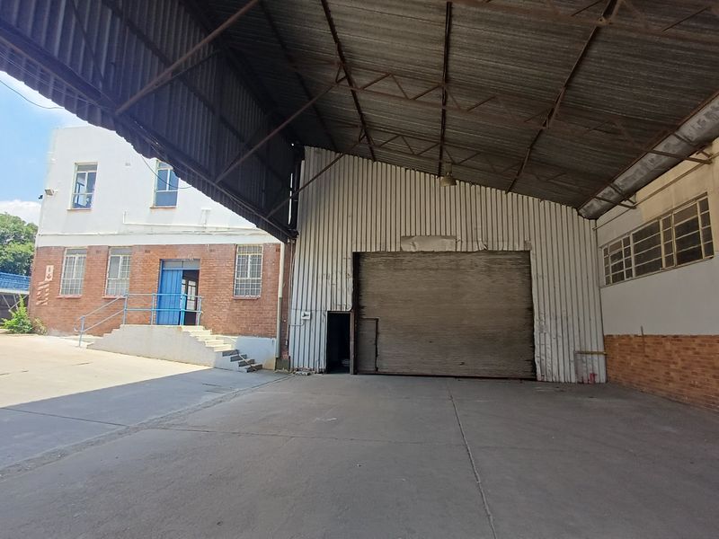 Industrial warehouse space featuring a large covered loading area, high-clearance metal roof, roller shutter door, and adjacent brick office or utility building.